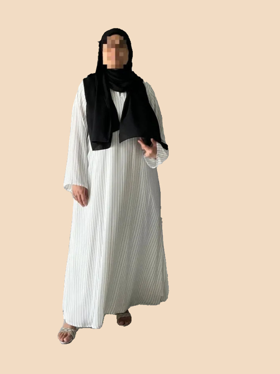 Woman wearing a pinstripe kaftan of premium fabric, styled with a black scarf, in an elegant indoor setting.